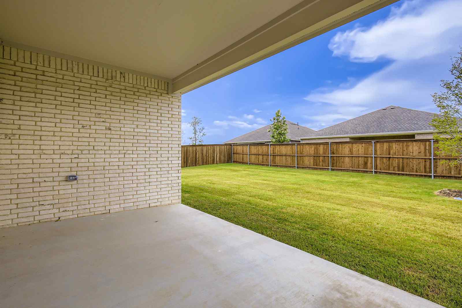 A fenced in yard with a brick wall and a grass field.