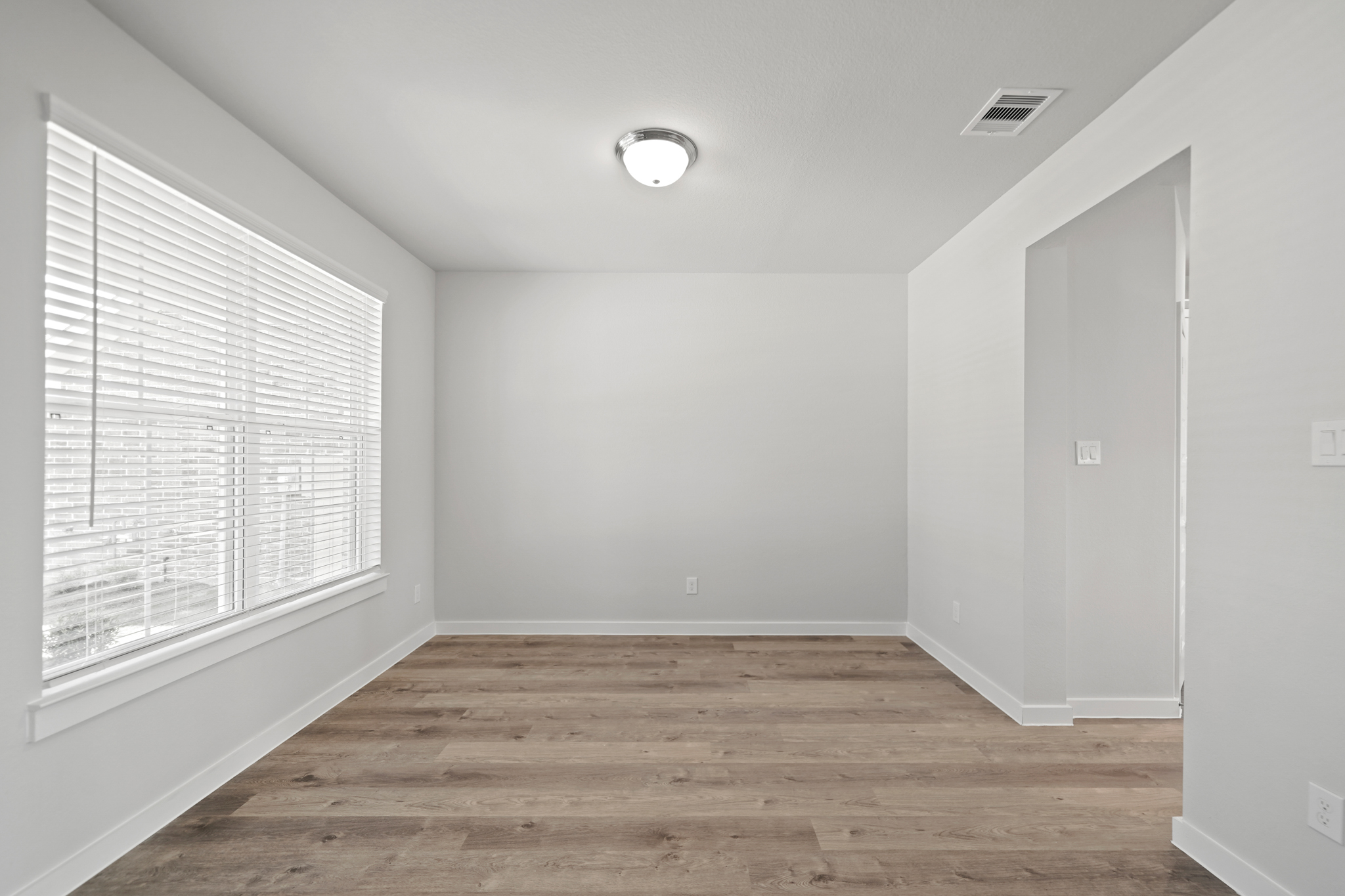 A room with a wood floor and a white wall with a light.