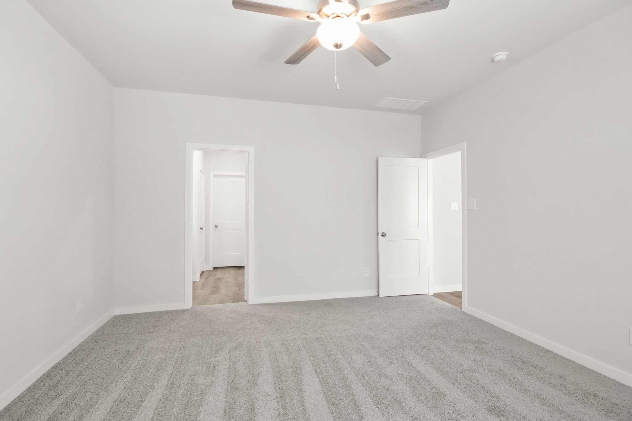 A room with a ceiling fan and white walls.