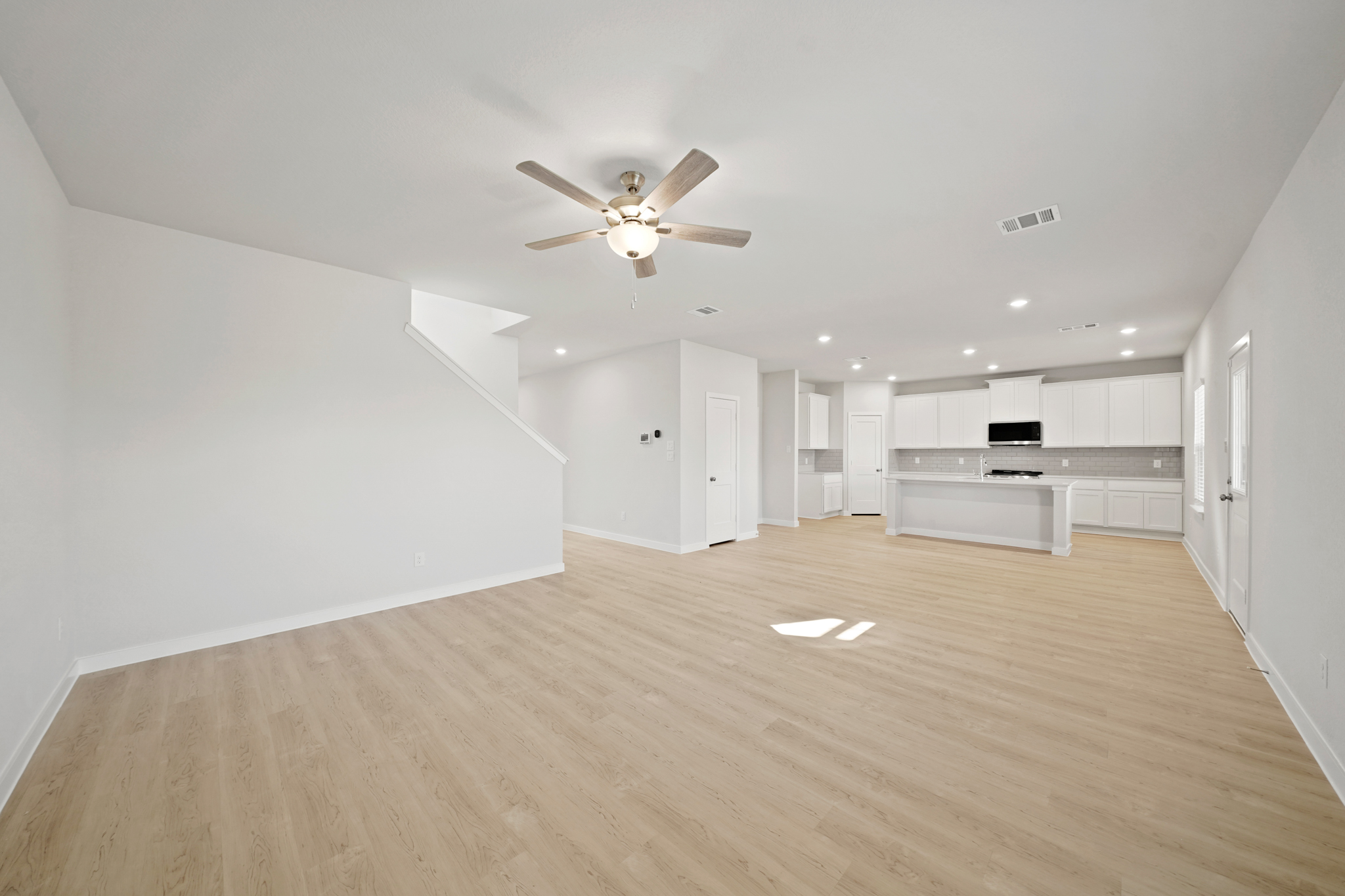A large empty room with a ceiling fan and white walls.