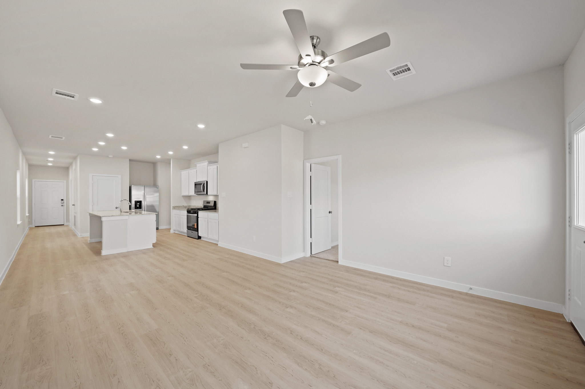 A large empty room with a ceiling fan and a wood floor.